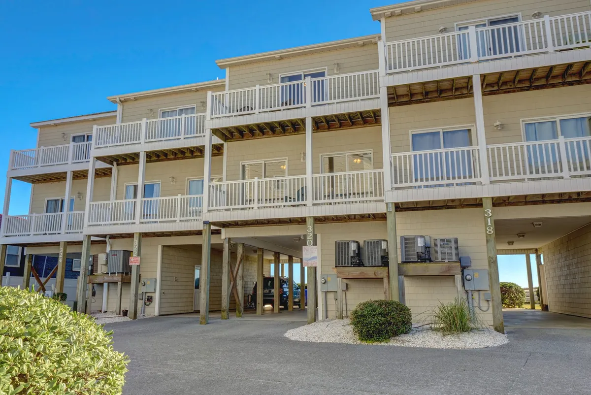 The exterior of the building is shown with visible balconies and a pathway leading up to the entrance. The scene evokes the anticipation of arrival and hints at easy access to nearby amenities like the beach path.