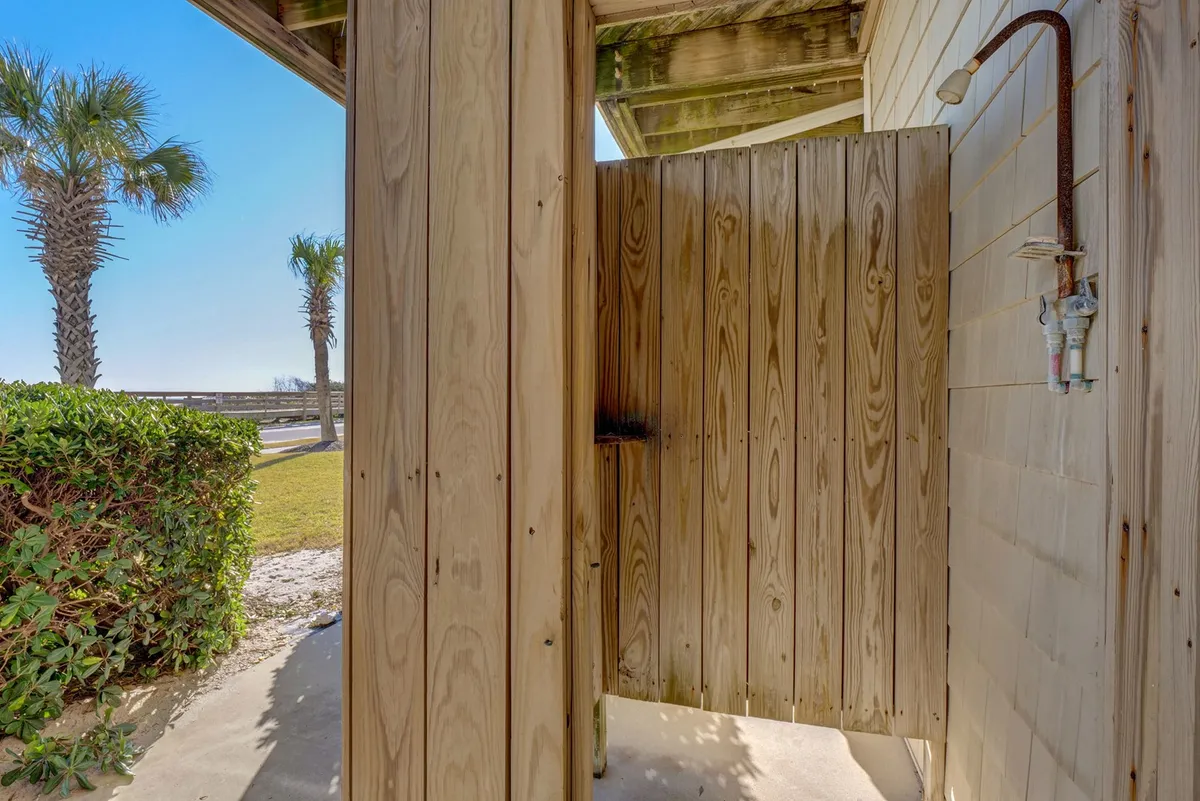 This image showcases a private outdoor shower set against a wooden privacy wall, surrounded by lush tropical palm trees and green shrubbery. The shower area is inviting and functional, emphasizing convenience for guests returning from the beach.