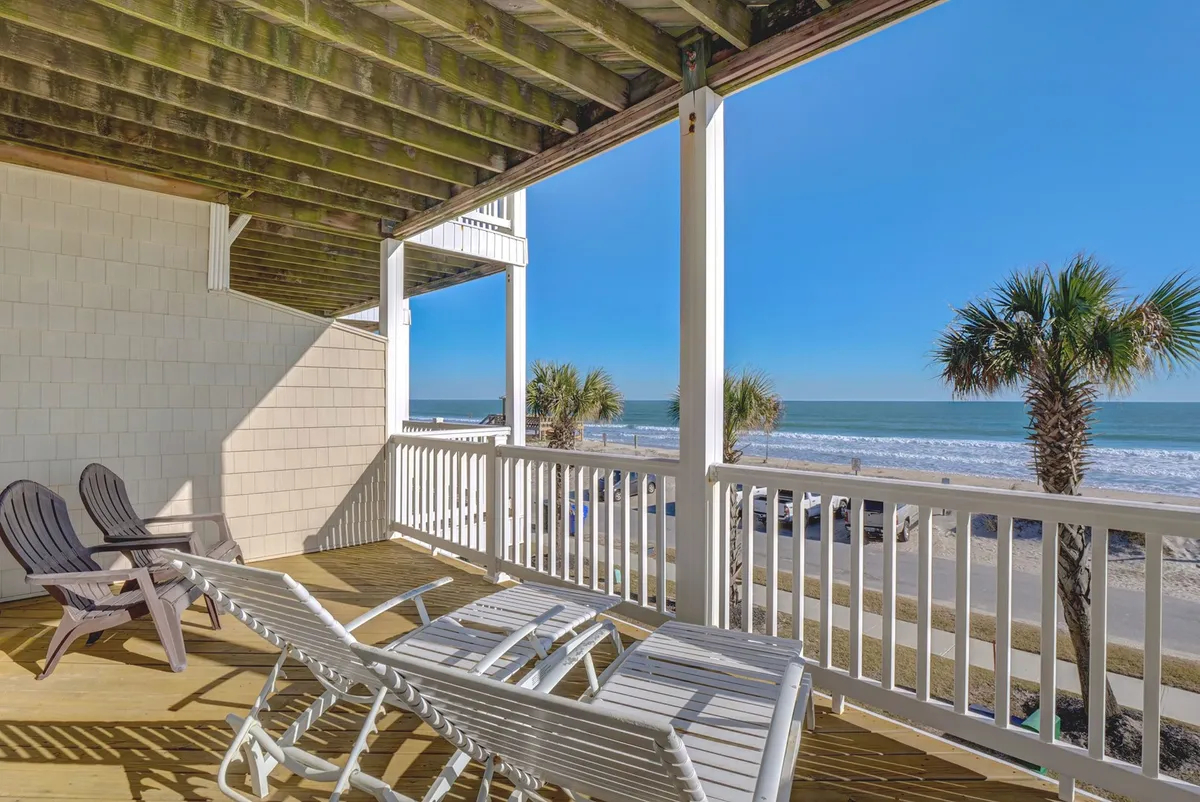 This exterior scene presents Adirondack chairs perfectly positioned on a beachfront deck, framed by palm trees and overlooking the expansive ocean. The setting invites relaxation and provides a clear sense of the property's direct connection to the beach.