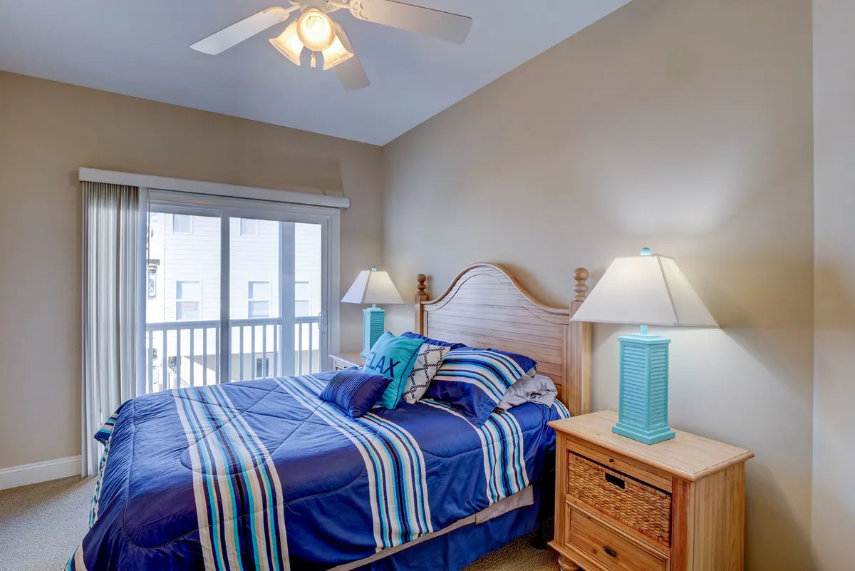 A peaceful bedroom with striped bedding, two bedside lamps, and a large window with curtains. The window suggests a view outward, inviting moments of relaxation or sipping coffee while enjoying the surrounding scenery.