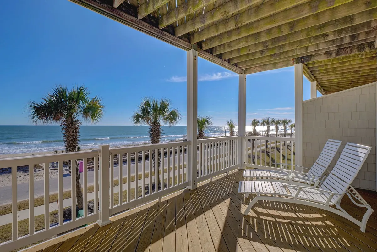 An exterior beachfront view with white lounge chairs lined up under palm trees, facing gentle ocean waves. The atmosphere is serene yet inviting, and the area is clearly intended for communal relaxation and socializing with the soothing sound of the sea nearby.
