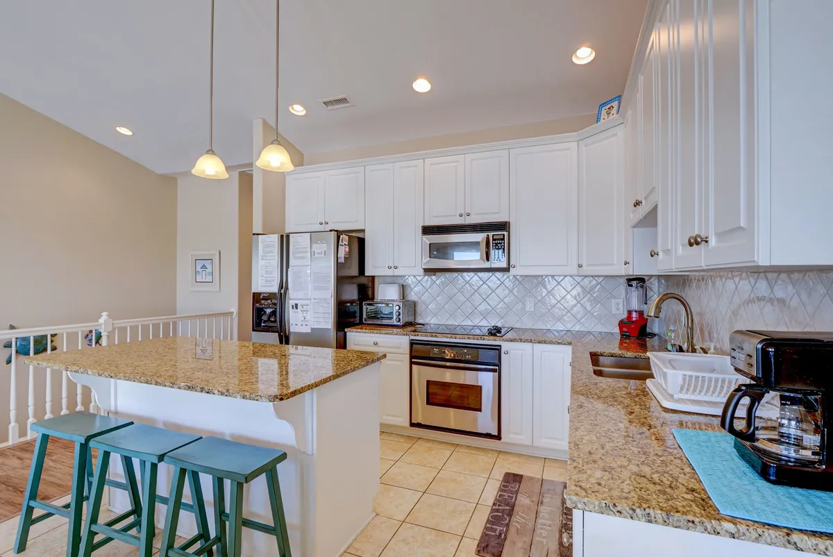 A modern kitchen with a granite island and stainless steel appliances, surrounded by light-filled windows. Stools at the island invite casual dining and socializing, while the open layout hints at lively gatherings before or after outings in town.