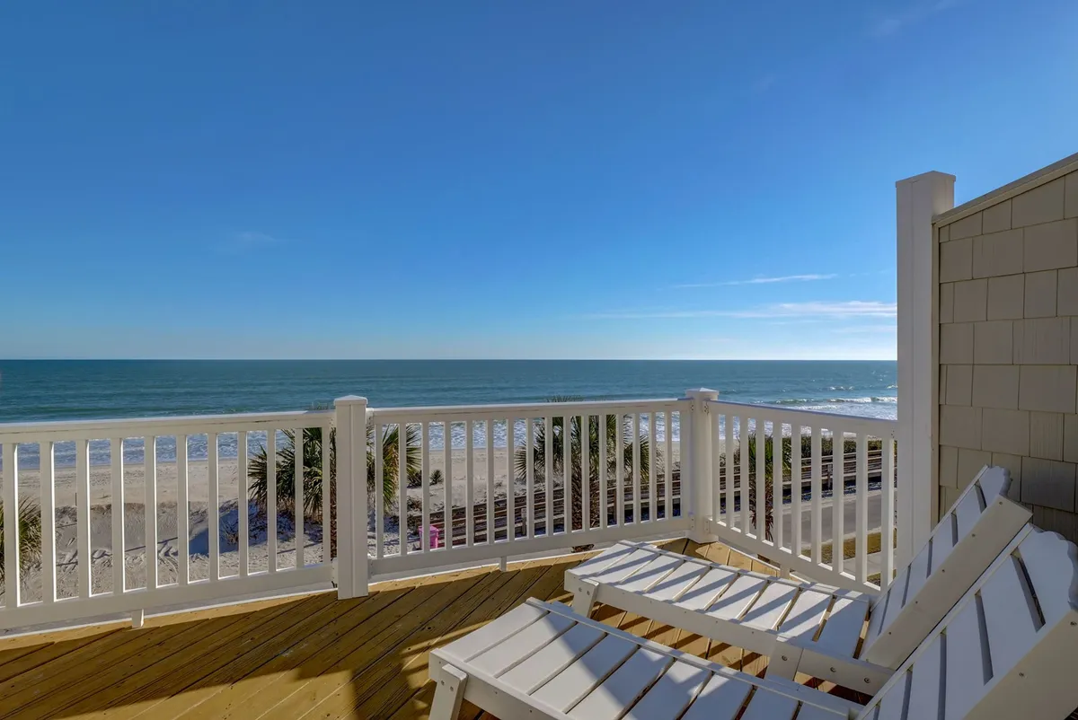 The hero image showcases a tranquil beachfront scene with crisp white lounge chairs arranged on a spacious deck overlooking the endless blue ocean and under a wide, clear sky. The inviting setup hints at leisurely activities such as sunbathing, reading, and soaking up mesmerizing sunrises or sunsets—all with the soothing soundtrack of the waves. The overall mood is serene and relaxing, highlighting the unique experience of private oceanfront living.