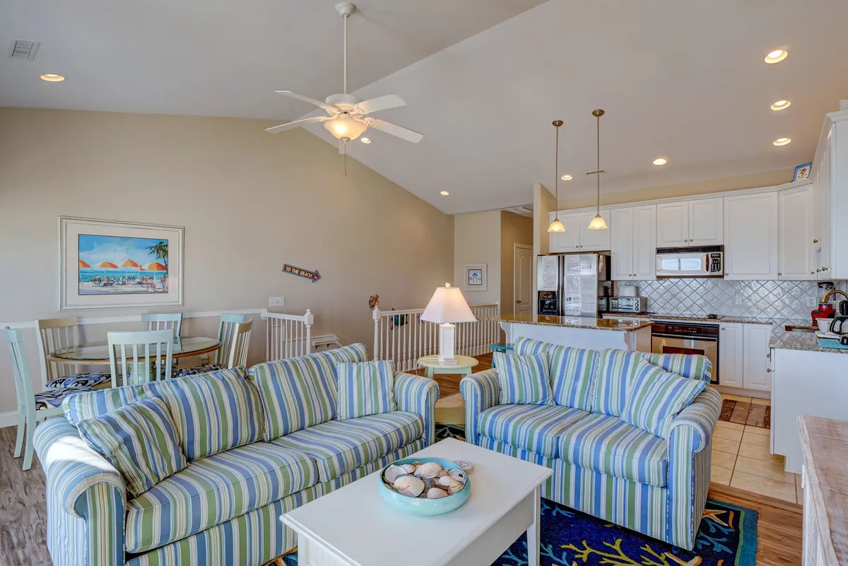 A cozy and inviting interior featuring striped sofas, a dining area, kitchen appliances, and a decorative painting. The arrangement suggests space for entertaining, relaxing, and group meals, highlighting a thoughtfully designed communal hub.