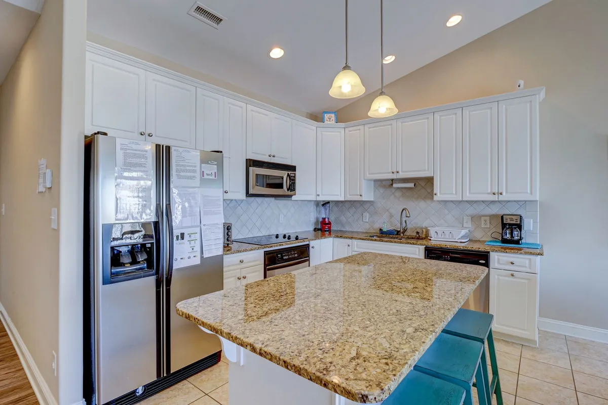 A welcoming kitchen with a granite island countertop, stainless steel appliances, white cabinetry, and pendant lighting. The space is designed for gathering, sharing meals, and creating memorable moments with family or friends. While not directly outside, the kitchen’s communal feel and reference to morning coffee or family meals support the section’s communal themes.