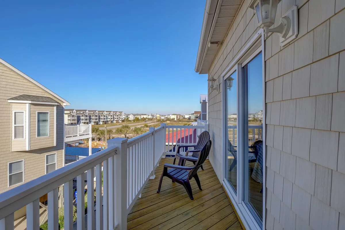 A peaceful balcony scene with wooden chairs looking out over neighboring buildings. The balcony railing frames the view, and the setting suggests quiet moments for morning coffee or evening relaxation.