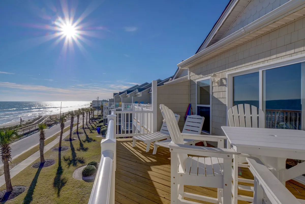An exterior shot from the private deck, featuring deck chairs and unobstructed ocean views with sunlight and palm trees. It shows the seamless transition from interior comfort to outdoor serenity, promising tranquil mornings and spectacular sunsets.