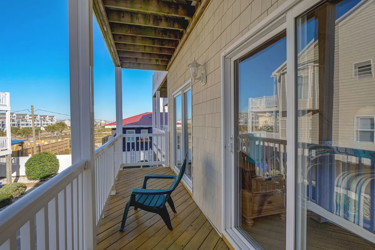 A tranquil balcony scene, with outdoor seating overlooking neighboring homes, offering a partial view of the surrounding coastal area. The mood is serene and invites quiet mornings or evenings enjoying the fresh air, with hints of the beach lifestyle visible in the architecture and landscaping.