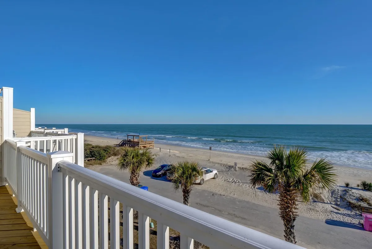 This image features a sweeping view of the ocean and beach, dotted with palm trees and a boardwalk leading directly to the sand. The tranquil shoreline is visible, with gentle waves meeting the golden sands, and the sky painted with soft sunrise or sunset hues.